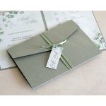 Zöld szalaggal átkötött esküvői meghívó monogram kártyával